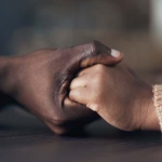 Close-up of two people holding hands across a table, with both wearing long-sleeved sweaters.