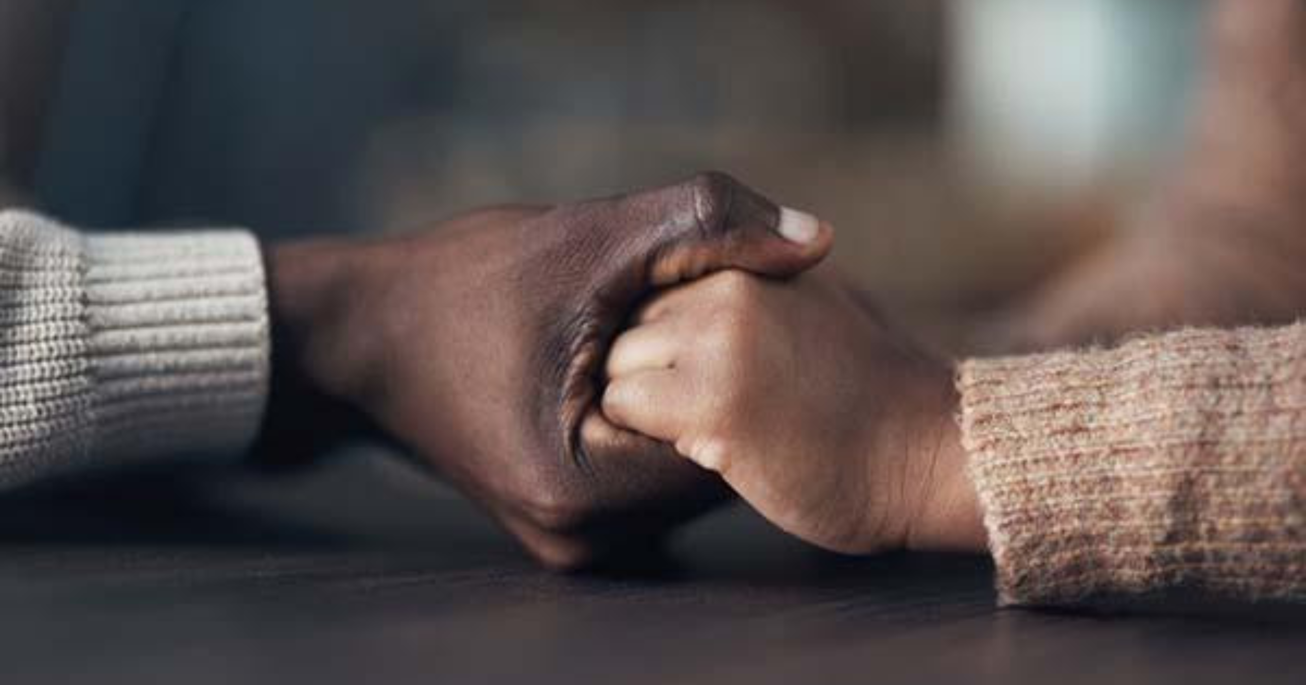 Close-up of two people holding hands across a table, with both wearing long-sleeved sweaters.
