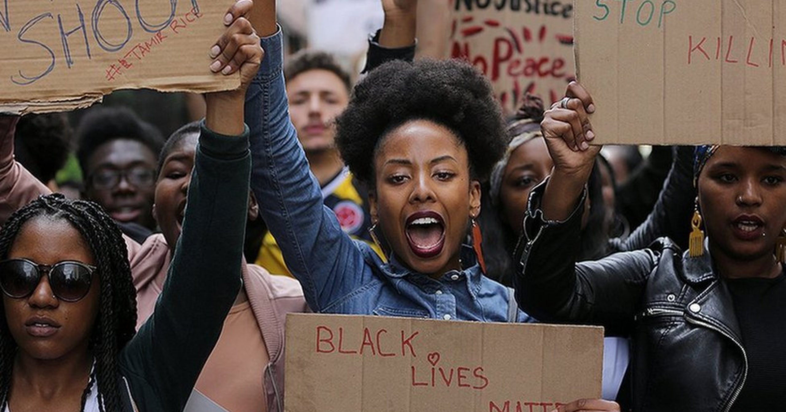 A group of people protest, holding signs with messages such as "Black Lives Matter" and raising fists in the air.