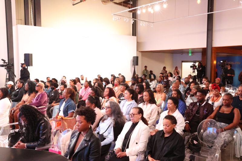 A diverse group of people seated and attentively listening at an indoor event or seminar with bright lighting.